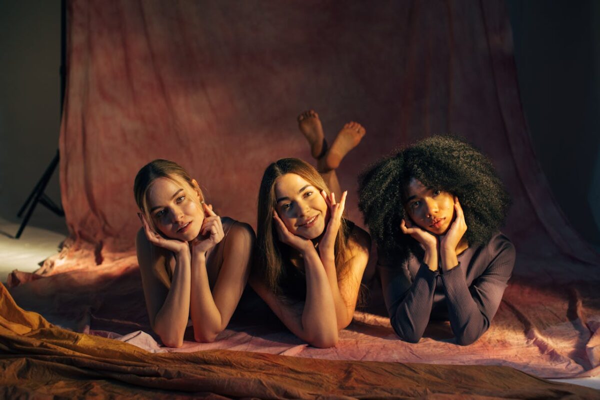 Three women posing playfully indoors, smiling in a studio setting.